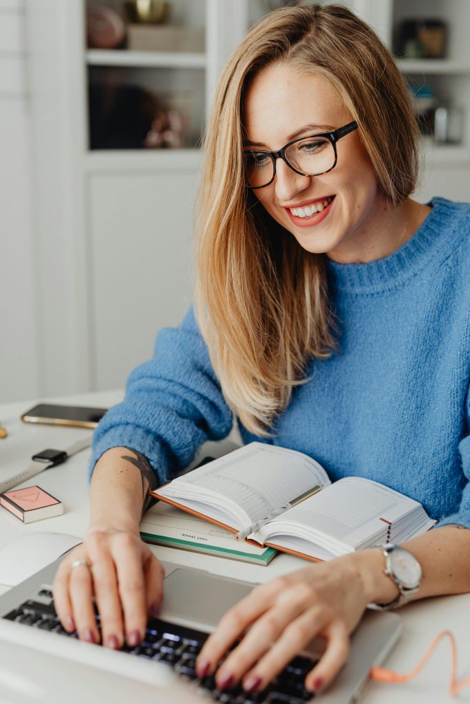 Soulution Coaching Silke Mekat pexels-photo-5908758-5908758 Smiling woman in eyeglasses typing on laptop at desk with open book.
