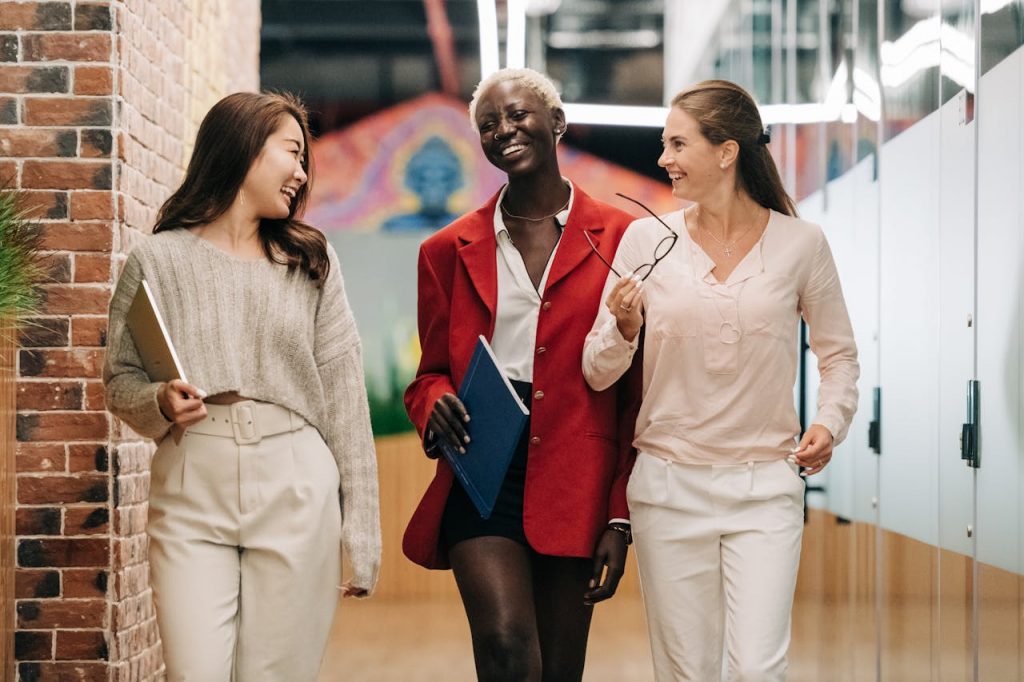 pexels-photo-6457562 Group of young glad businesswomen in trendy elegant outfits smiling and discussing business strategy in contemporary workspace